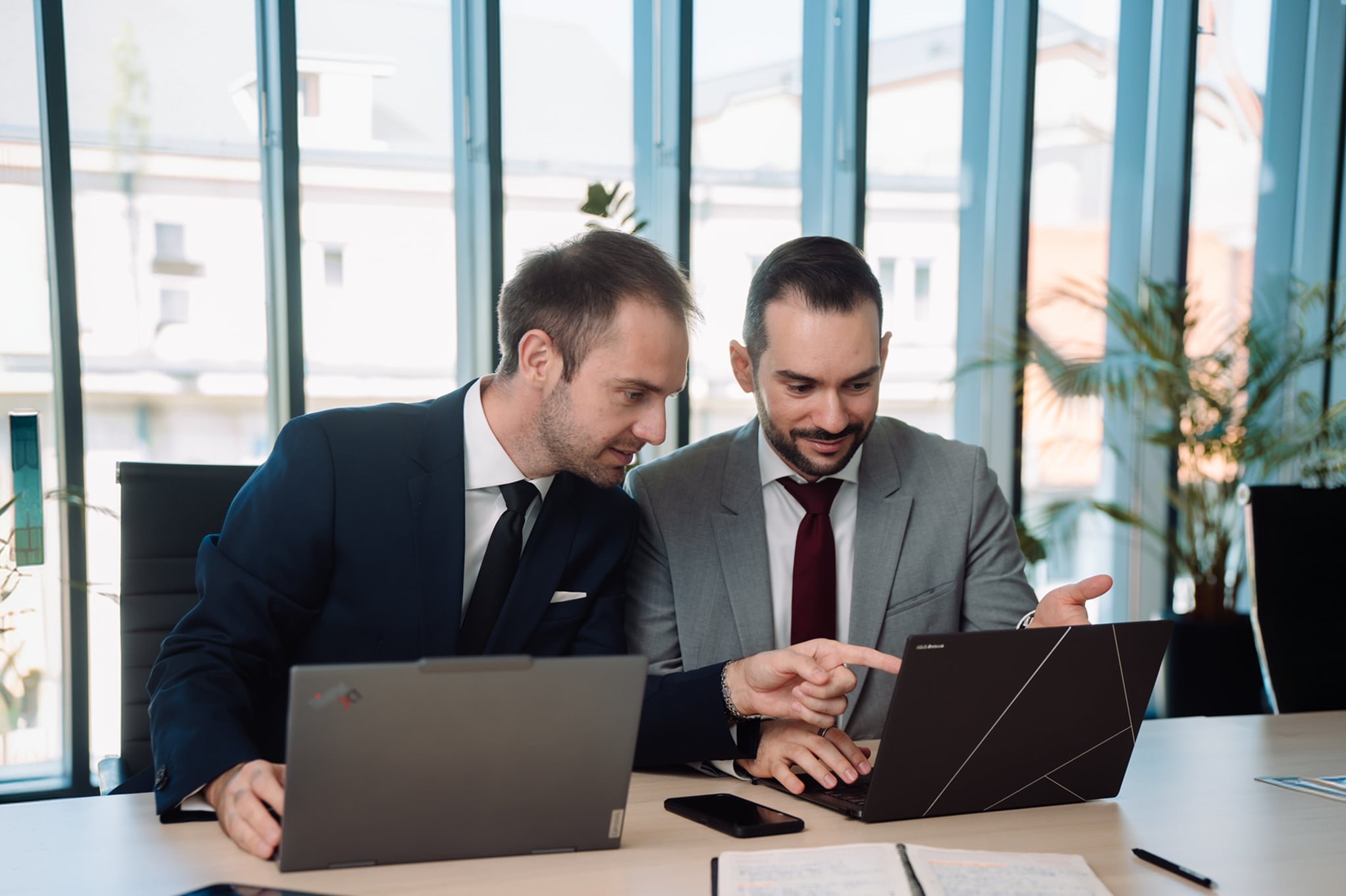 Two consultants discussing their work on laptops at a meeting table.